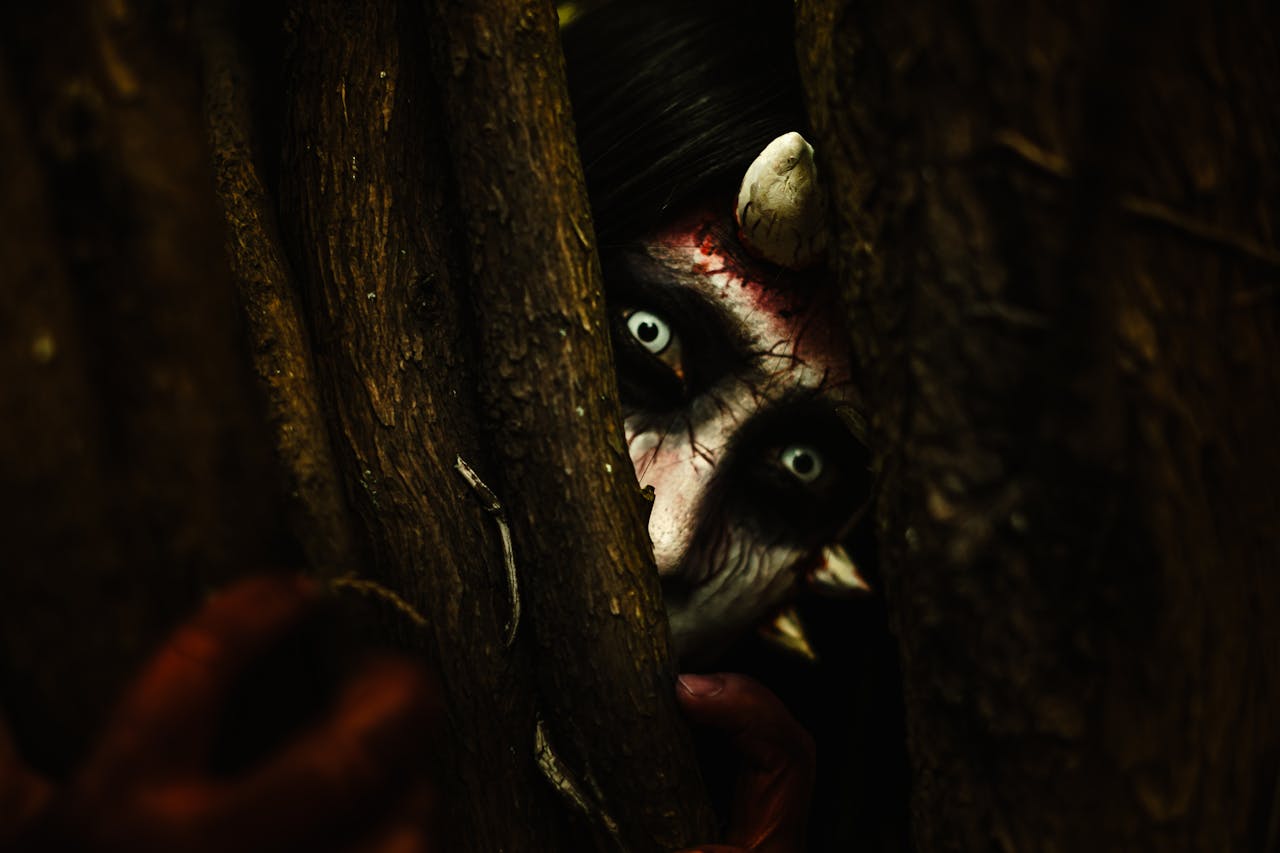 Mastering the First Impression: Your intriguing post title goes here A person with devilish makeup peers through tree branches, creating an eerie Halloween vibe.