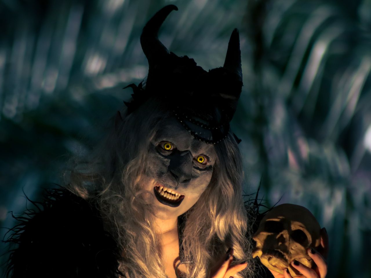 Menu A costumed figure with horns and yellow eyes holds a skull in a dark forest setting, creating a spooky vibe.